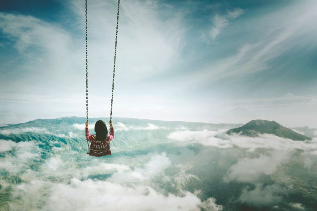 Little girl on a swing on top of the mountain overlooking the clouds