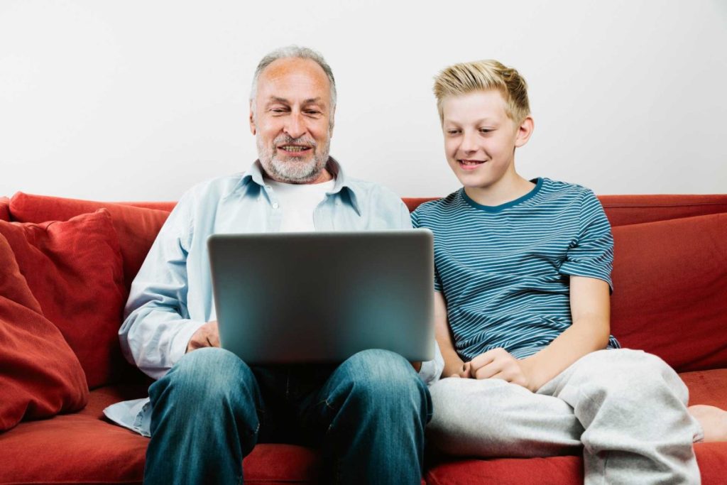 Elderly man and boy sitting on a red couch looking at a laptop