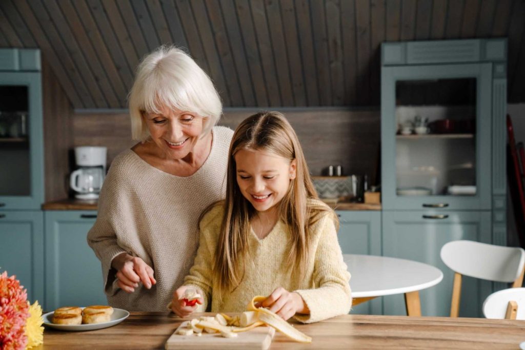 Elderly woman and young girl smiling while preparing snacks in a kitchen