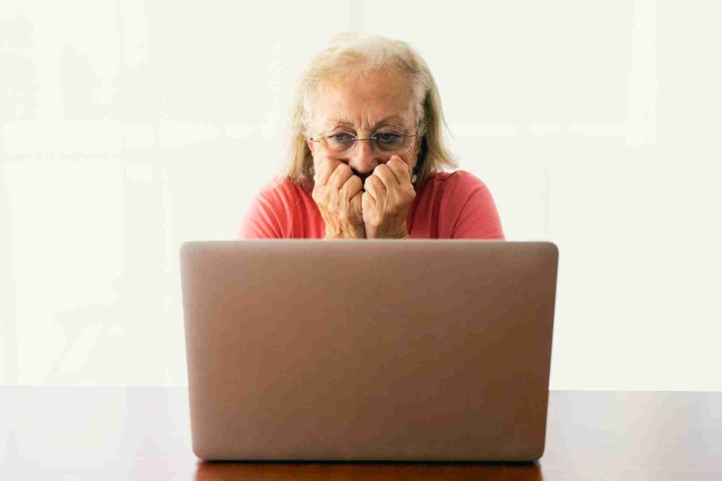 Elderly woman wearing glasses looking worried while using a laptop