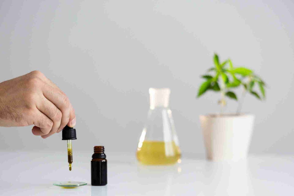 Hand using a dropper with CBD oil beside a small plant and glass beaker