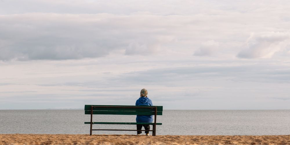 Lonely girl sitting on a bench facing a calm lake.