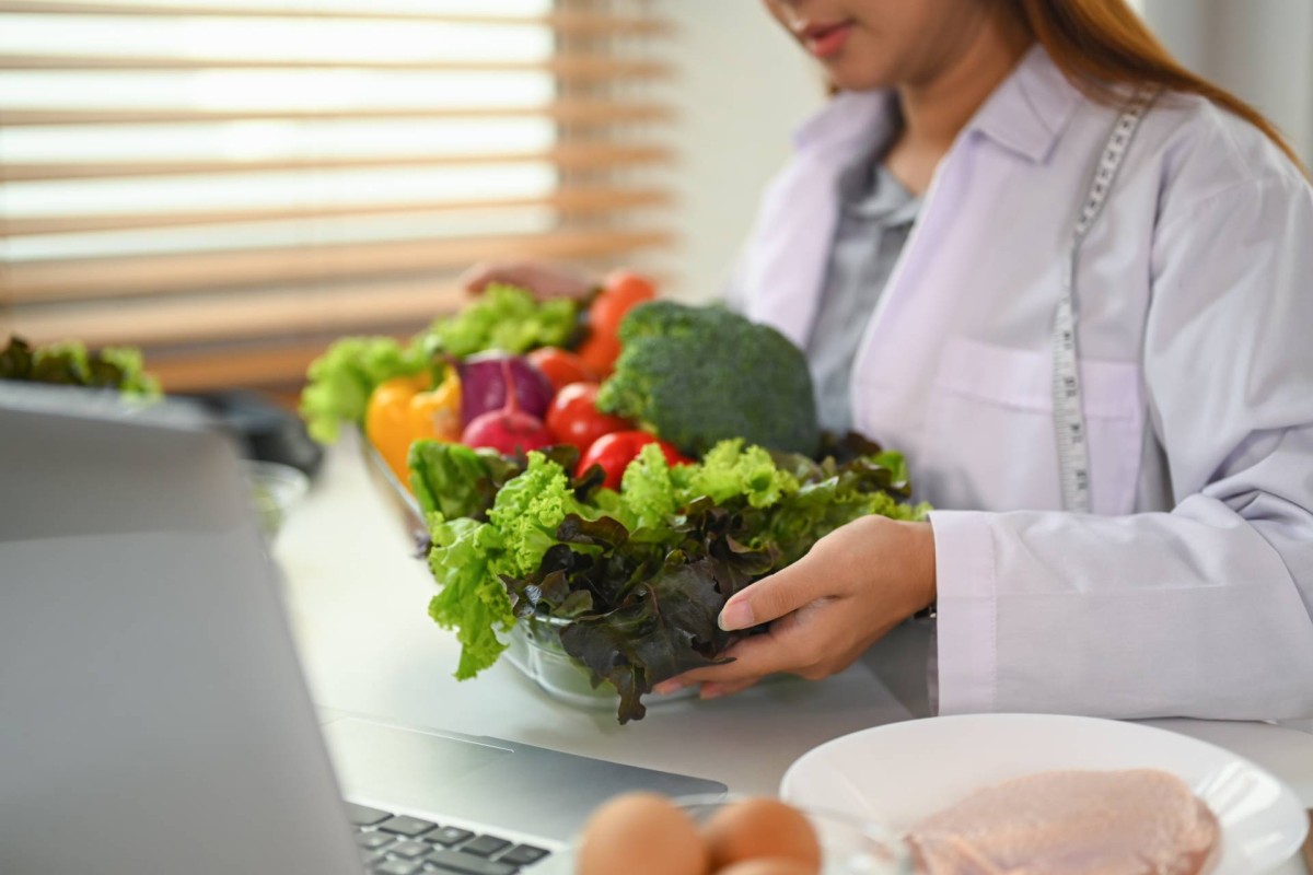 Nutritionist holding a bowl of fresh vegetables in front of a laptop