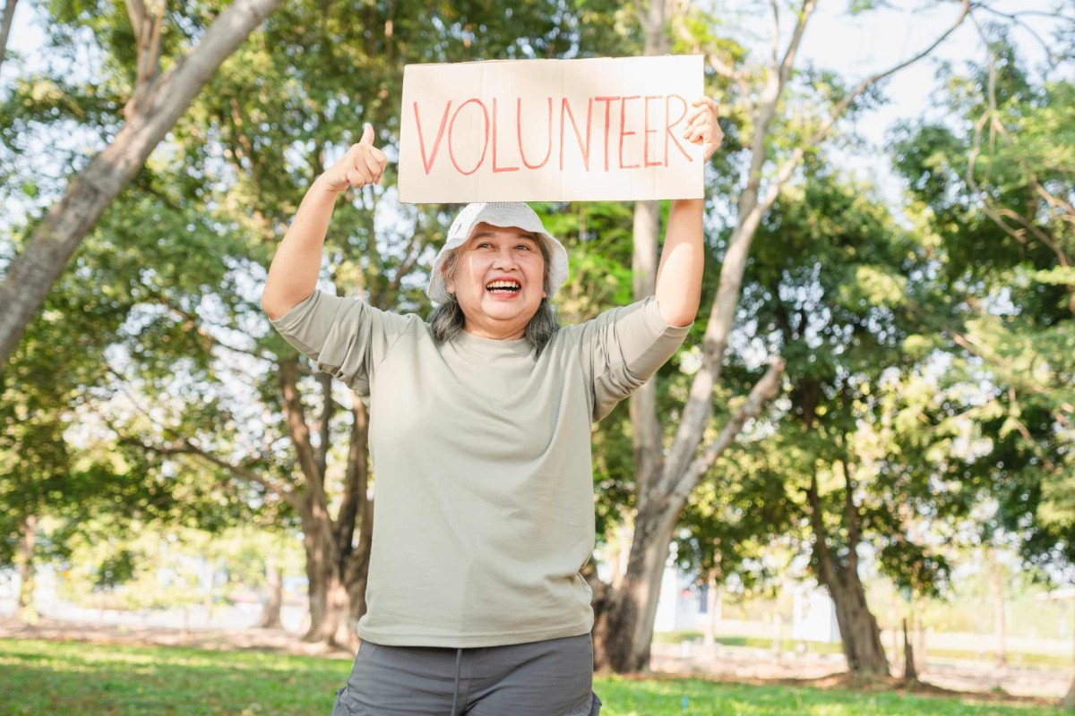 Smiling woman holding a volunteer sign outdoors