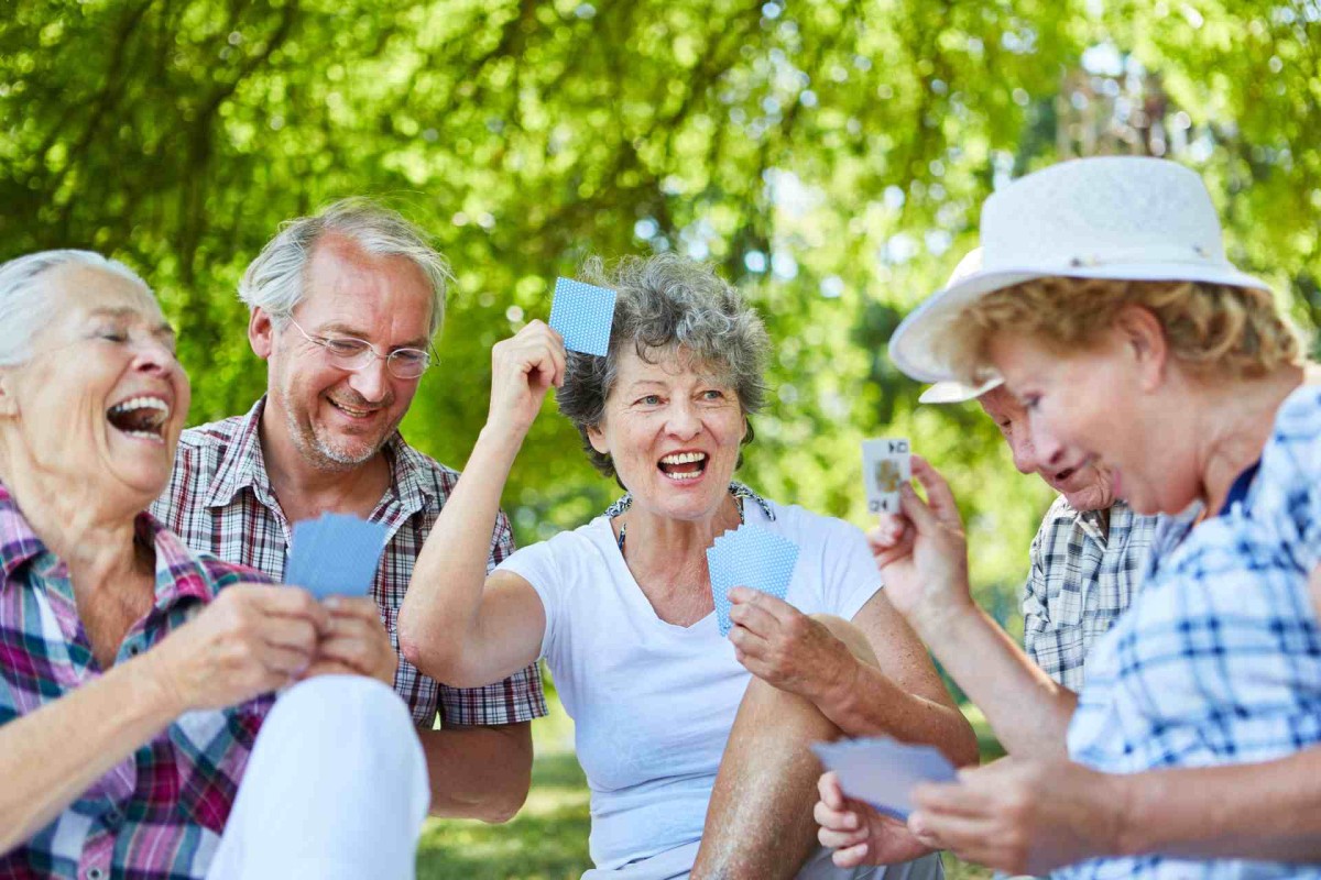 Group of seniors laughing and playing cards in a sunny park
