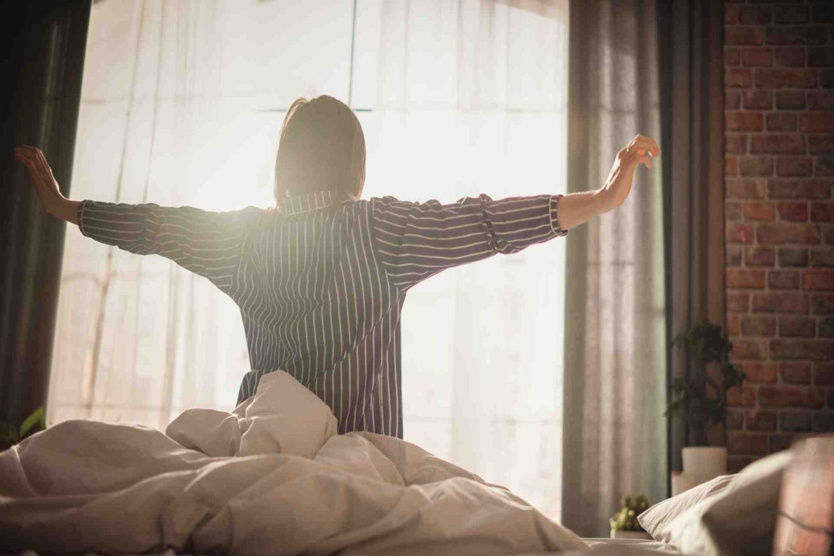Person stretching arms in bed with sunlight streaming through a window