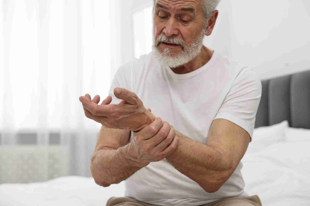 Older man holding and rubbing his wrist in pain while sitting on a bed
