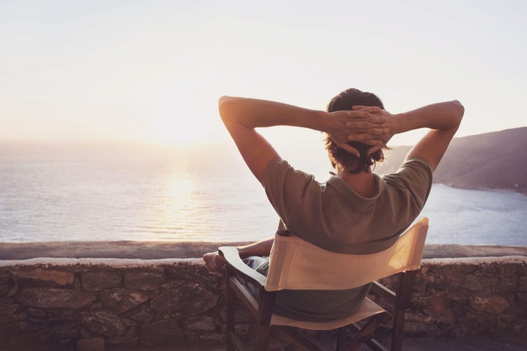 A guy sitting on a chair by the beach enjoying the sunset. 